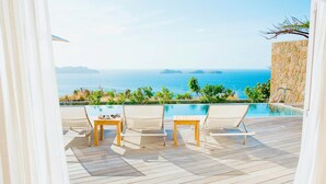 Una terraza de madera con piscina, sillas y una mesa con vista al mar.