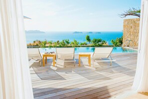 Eine Holzterrasse mit Pool, Stühlen und einem Tisch mit Blick auf das Meer.
