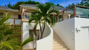Una casa moderna con una escalera curva que conduce a un balcón, rodeada de palmeras.