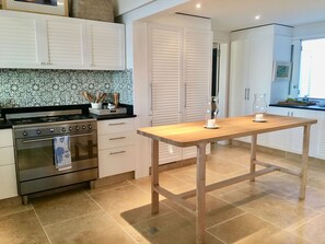 A kitchen with a wooden table, white cabinets, a stove, and a patterned backsplash. - Villa Marie (2 bedrooms) (Saint Barthélemy)