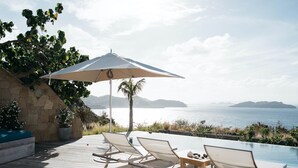 Eine Holzterrasse mit Liegestühlen und einem Tisch, mit Blick auf einen Pool und die malerische Seeblick.