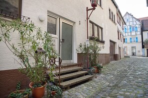 A cobblestone street with a building featuring a door, window, and steps leading to a balcony.