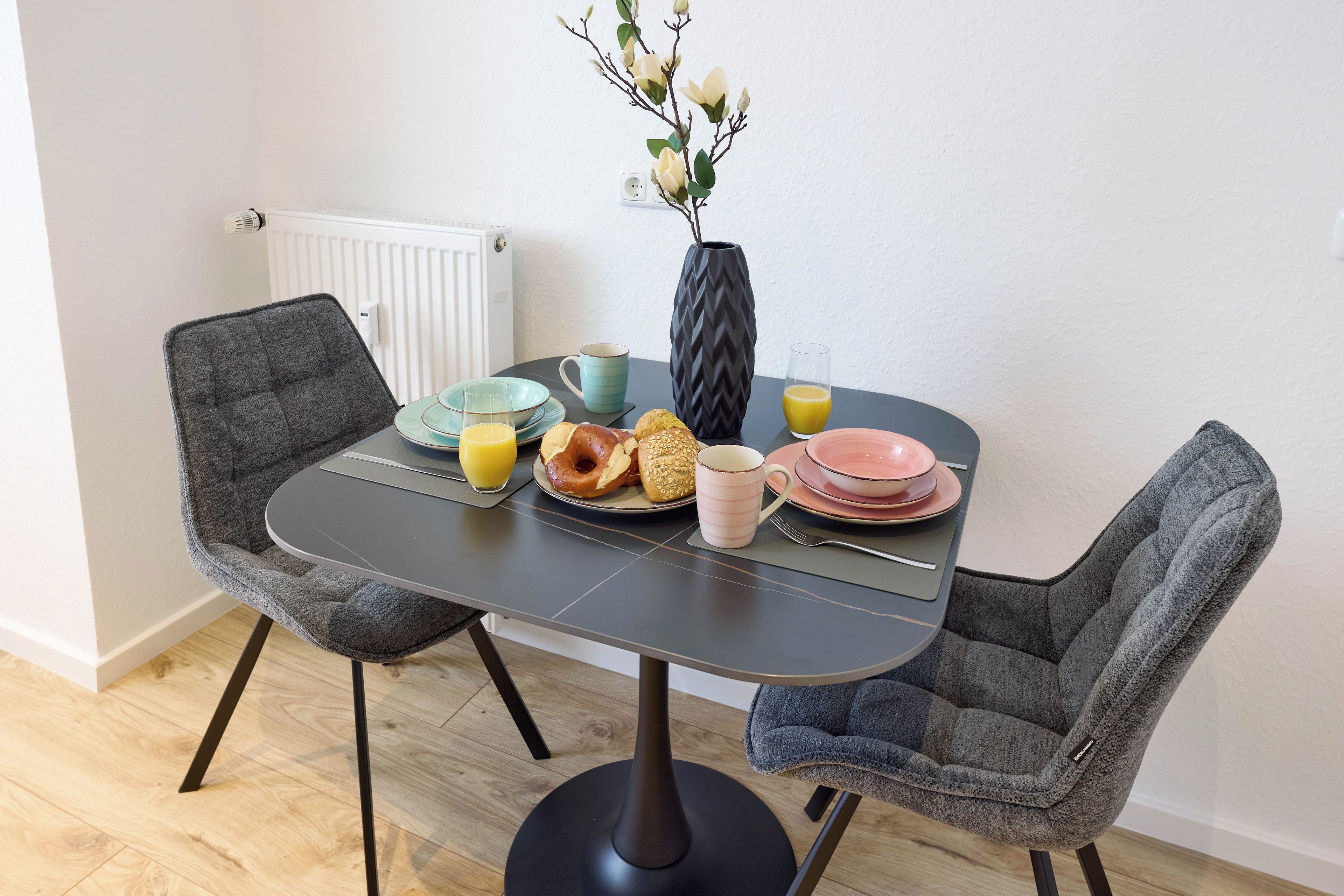 A dining table with chairs, plates, a mug, and a glass of orange juice.