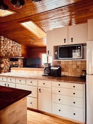 A kitchen with wooden ceiling beams, a stone wall, and a built-in microwave.