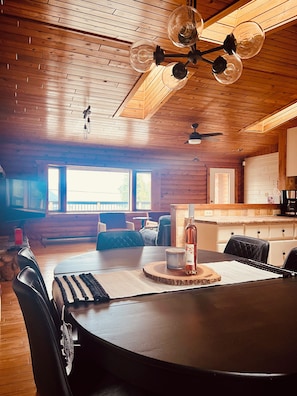 A wooden interior with a dining table, chairs, a ceiling fan, and a kitchen area.