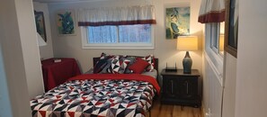 Quarto com cama, mesa de cabeceira, luminária, janela com cortinas e obras de arte nas paredes.