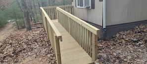 A wooden deck leading to a building with an air conditioning unit mounted on the exterior wall.