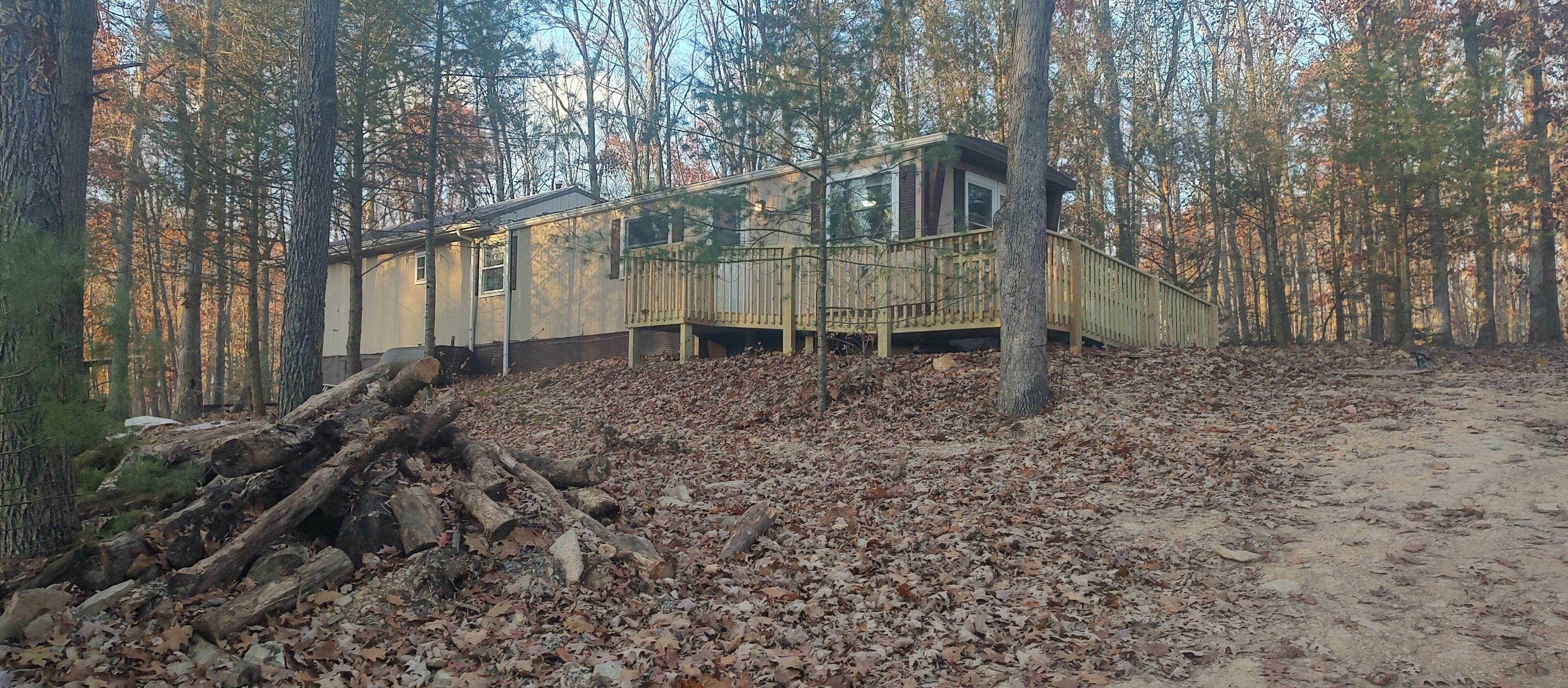 Una cabaña con terraza de madera y una escalera que lleva a un porche, rodeada por un bosque de hojas caídas.