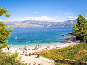 A beach with clear blue water, people sunbathing, and boats in the distance. - One Bedroom Apartment with Terrace an Sea View (Postira)