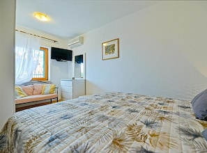 Ein Schlafzimmer mit Bett, Schreibtisch, Stuhl, einem Fenster mit Vorhängen und einer Wand-Klimaanlage.