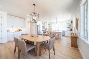 A modern kitchen with white cabinetry, a central island, and a dining area with a round table and chairs. - Seascape Haven, Modern Townhome with Fireplace (Depoe Bay)