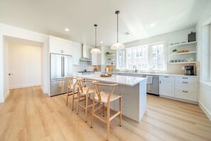 A modern kitchen with a central island, bar stools, and a large window providing natural light. - Seascape Haven, Modern Townhome with Fireplace (Depoe Bay)