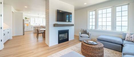 A modern living room with a fireplace, a television mounted on the wall, and a large window providing a view of the outside.