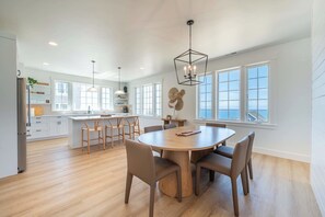 A spacious kitchen with a central island, large windows, and a dining area with a round table and chairs. - Seascape Haven, Modern Townhome with Fireplace (Depoe Bay)