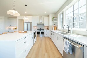 A modern kitchen with white cabinetry, a stainless steel refrigerator, a double oven, and a large window providing natural light. - Seascape Haven, Modern Townhome with Fireplace (Depoe Bay)