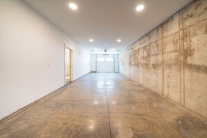 A long, empty hallway with a concrete floor and white walls, leading to a garage door. - Seascape Haven, Modern Townhome with Fireplace (Depoe Bay)