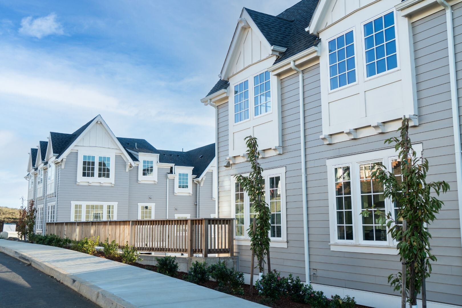 Une rangée de maisons de ville modernes, toutes conçues dans un style architectural uniforme, avec de grandes fenêtres et un jardin avant bien entretenu.