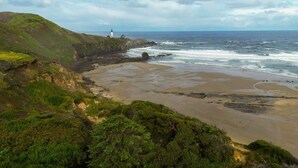 A coastal landscape with a lighthouse, sandy beach, and green hills. - Seascape Lookout Townhome, Large Kitchen & Pet Friendly (Depoe Bay)