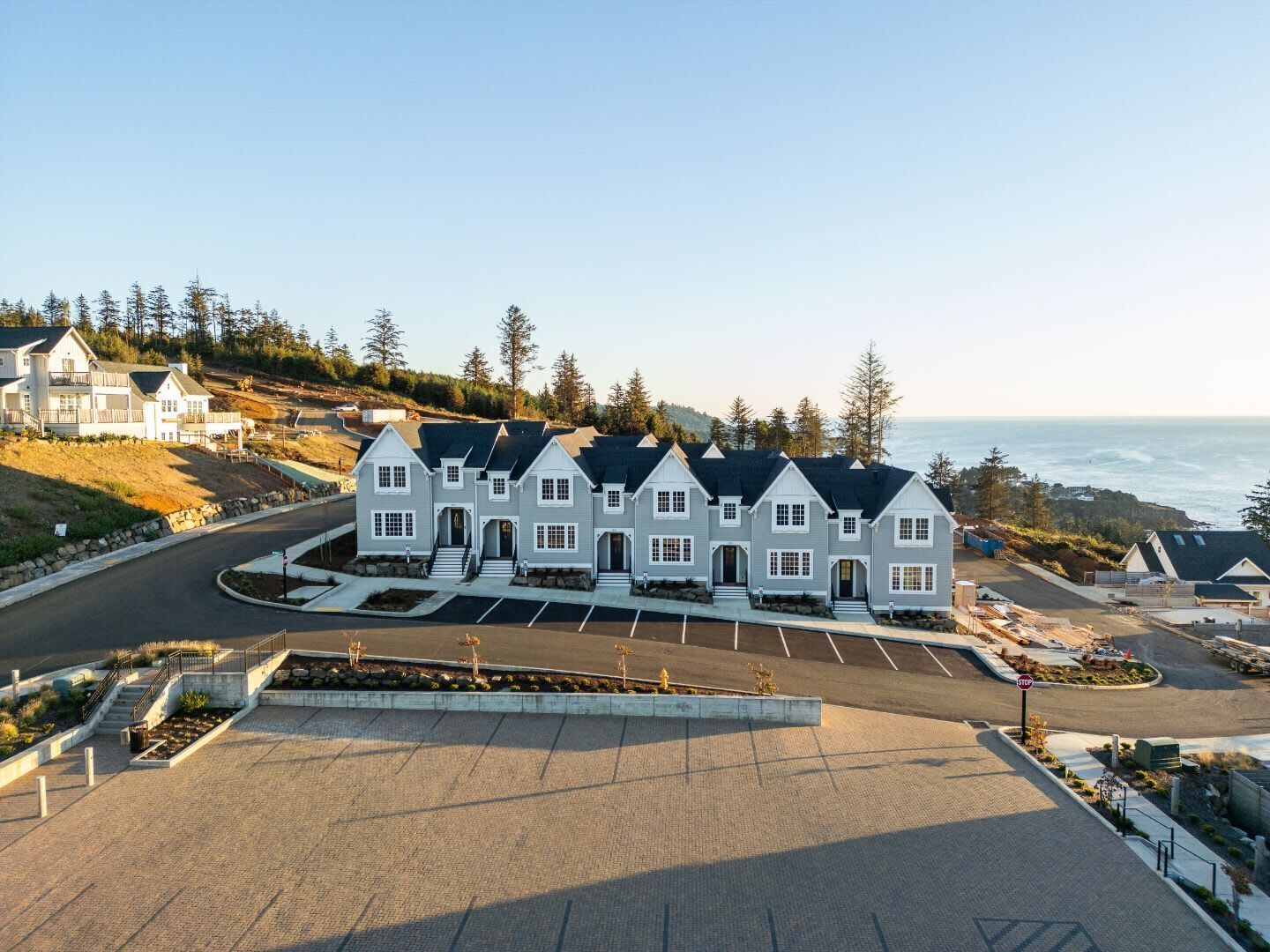 Un área residencial costera con una hilera de casas de estilo arquitectónico uniforme, un camino pavimentado y un estacionamiento.