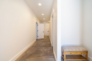 Un couloir étroit avec un banc, des murs blancs et une porte au fond.