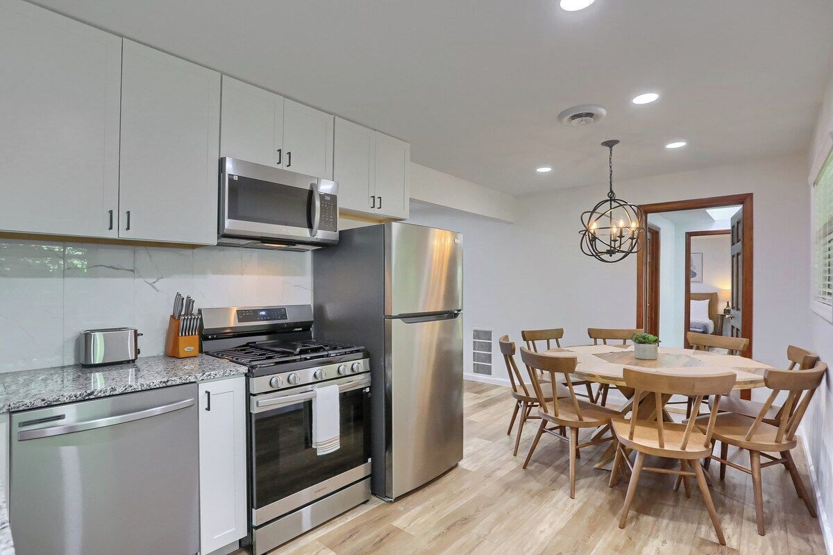 A modern kitchen with stainless steel appliances, wooden dining table, and chairs.