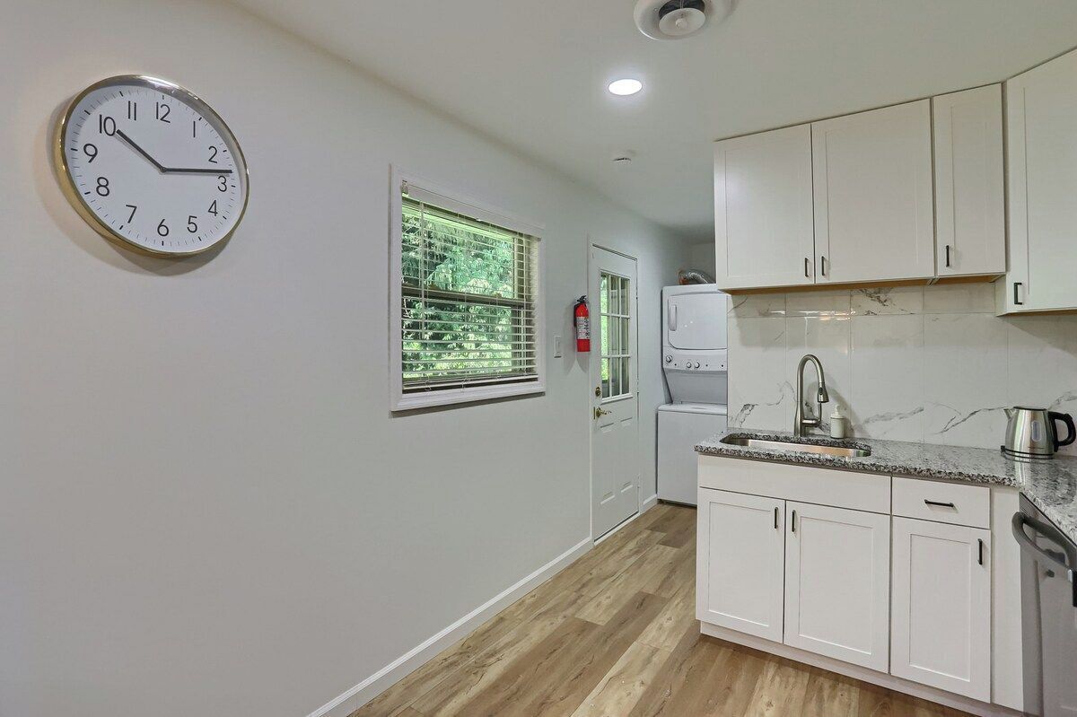 A kitchen with white cabinets, a stainless steel sink, and a clock on the wall.