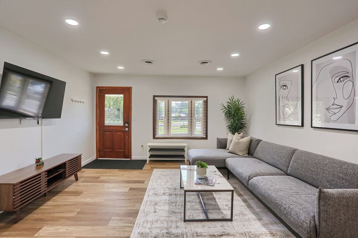 A modern living room with a grey sofa, a coffee table, a TV mounted on the wall, and a door with a window.