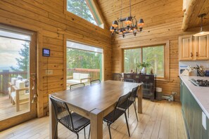 A wooden cabin interior with a dining table, chairs, a kitchen area, and large windows offering views of the outdoors. - Beautiful Dog Friendly Cabin in Fairplay (Fairplay)
