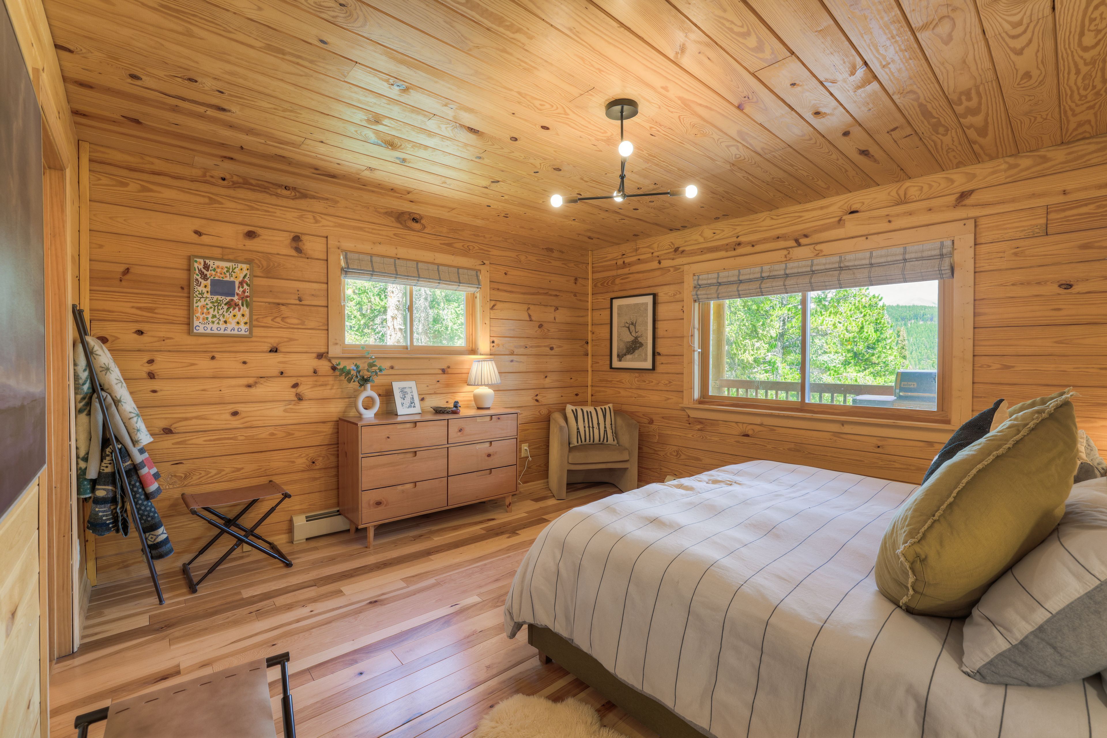 Ein Schlafzimmer in einer Holzhütte mit Bett, Kommode und Fenstern.