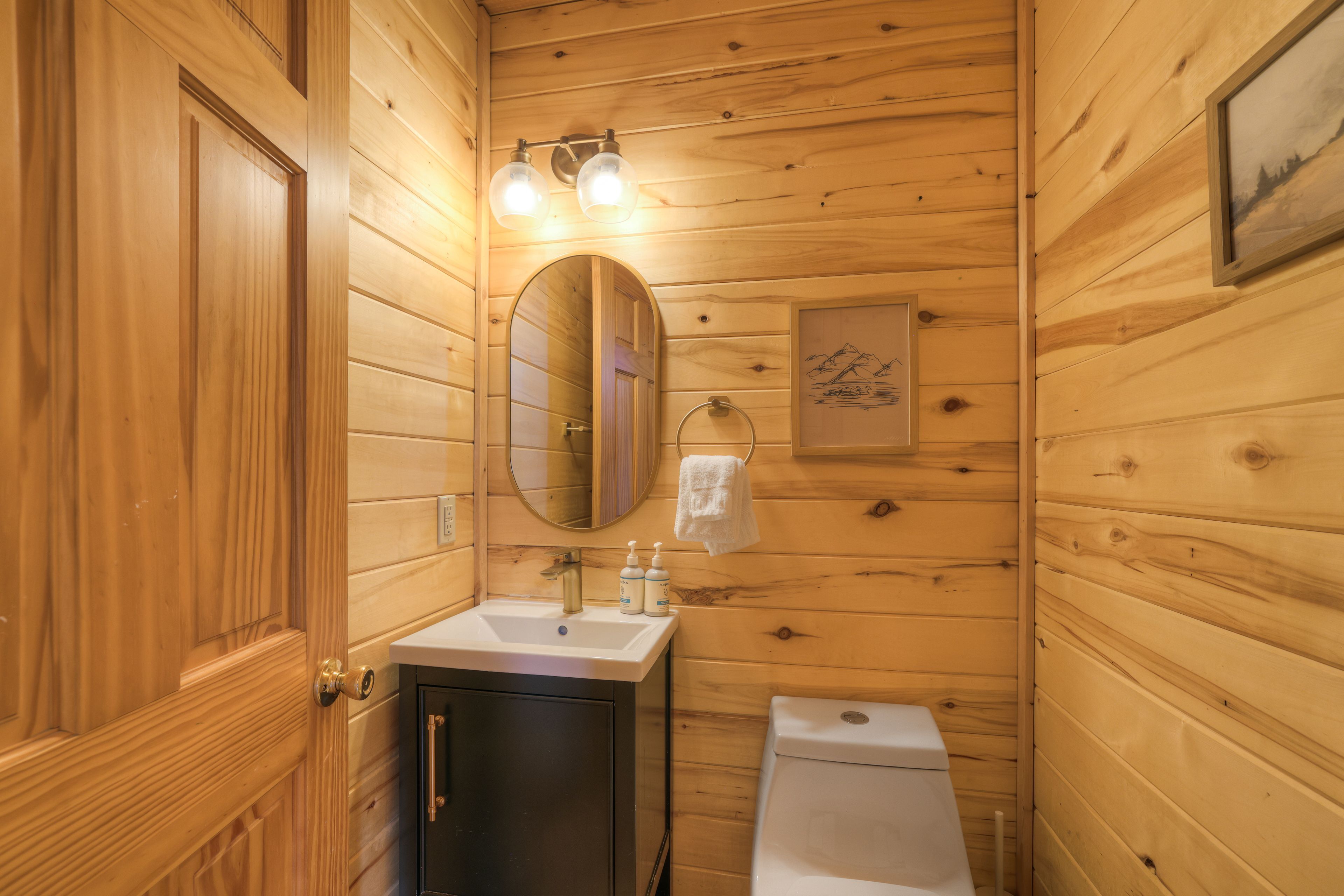 Une salle de bain rustique, aménagée dans une cabane en bois, comprenant un lavabo, un miroir, un porte-serviettes et des toilettes.