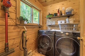 A laundry room with two front-loading washing machines, a red Dyson vacuum, and a window with a view of trees. - Beautiful Dog Friendly Cabin in Fairplay (Fairplay)