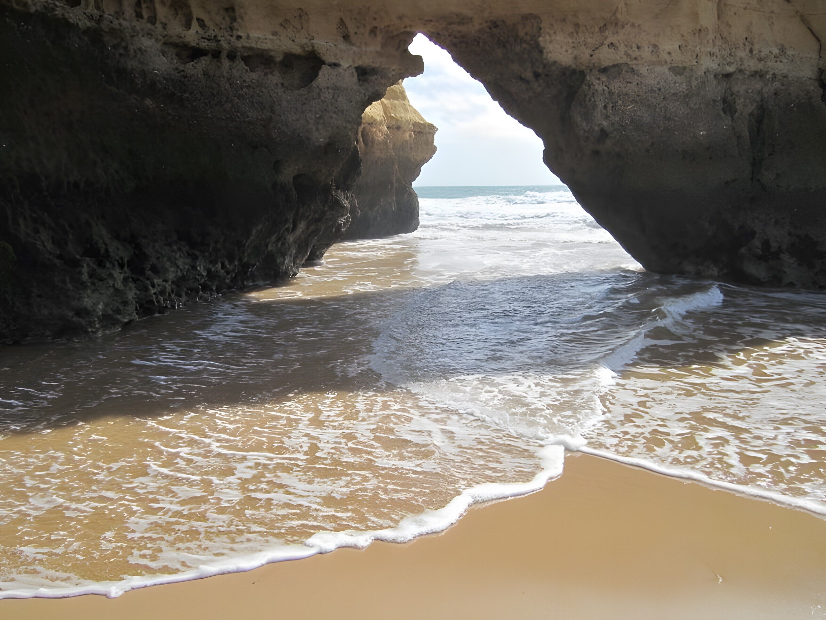 A beach with waves entering through a natural rock arch.