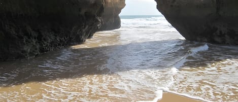 A beach with waves entering through a natural rock arch.