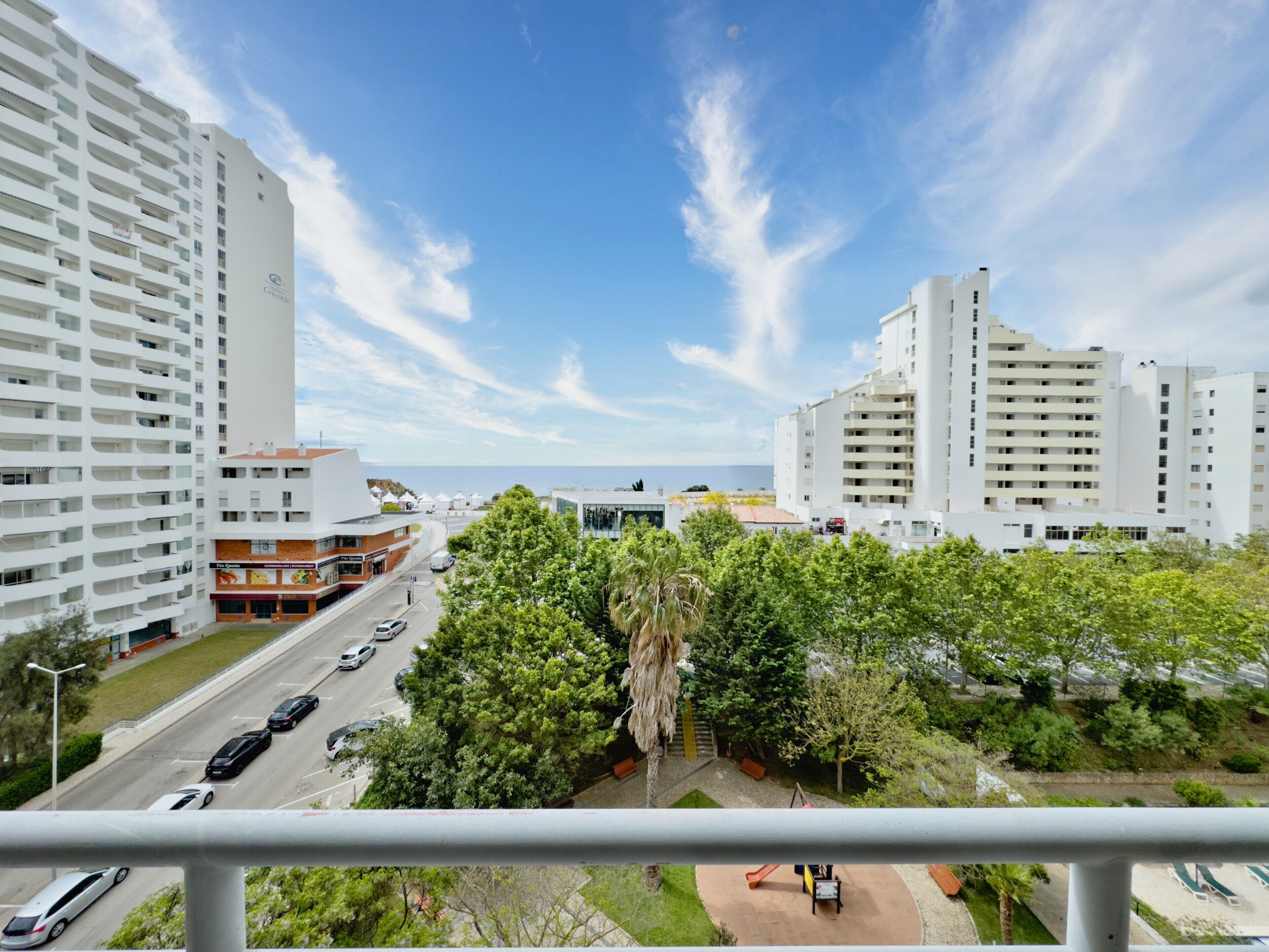 Un edificio alto con vista al mar, una calle con coches y un parque infantil.