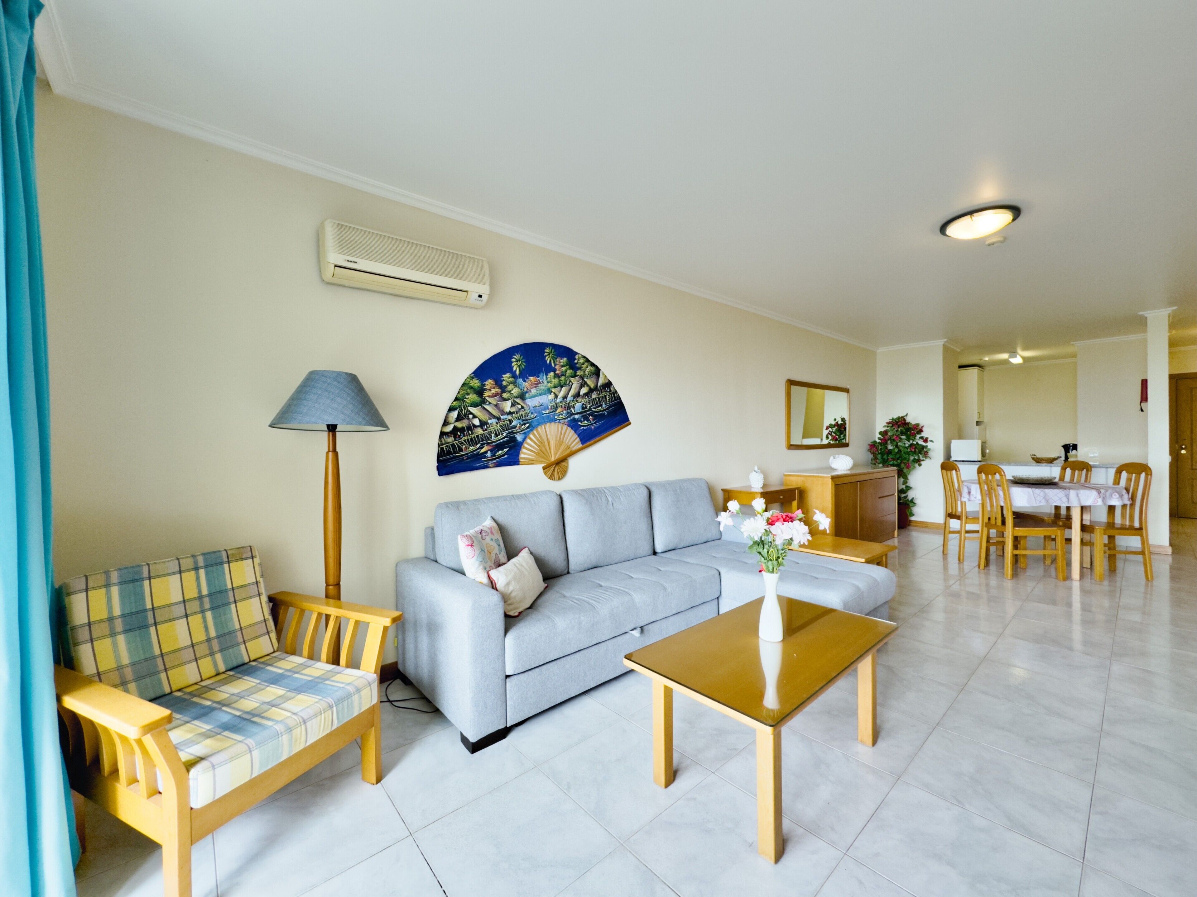 Uma sala de estar com um sofá, uma mesa de madeira, uma luminária e um espaço de refeições com cadeiras e uma mesa.