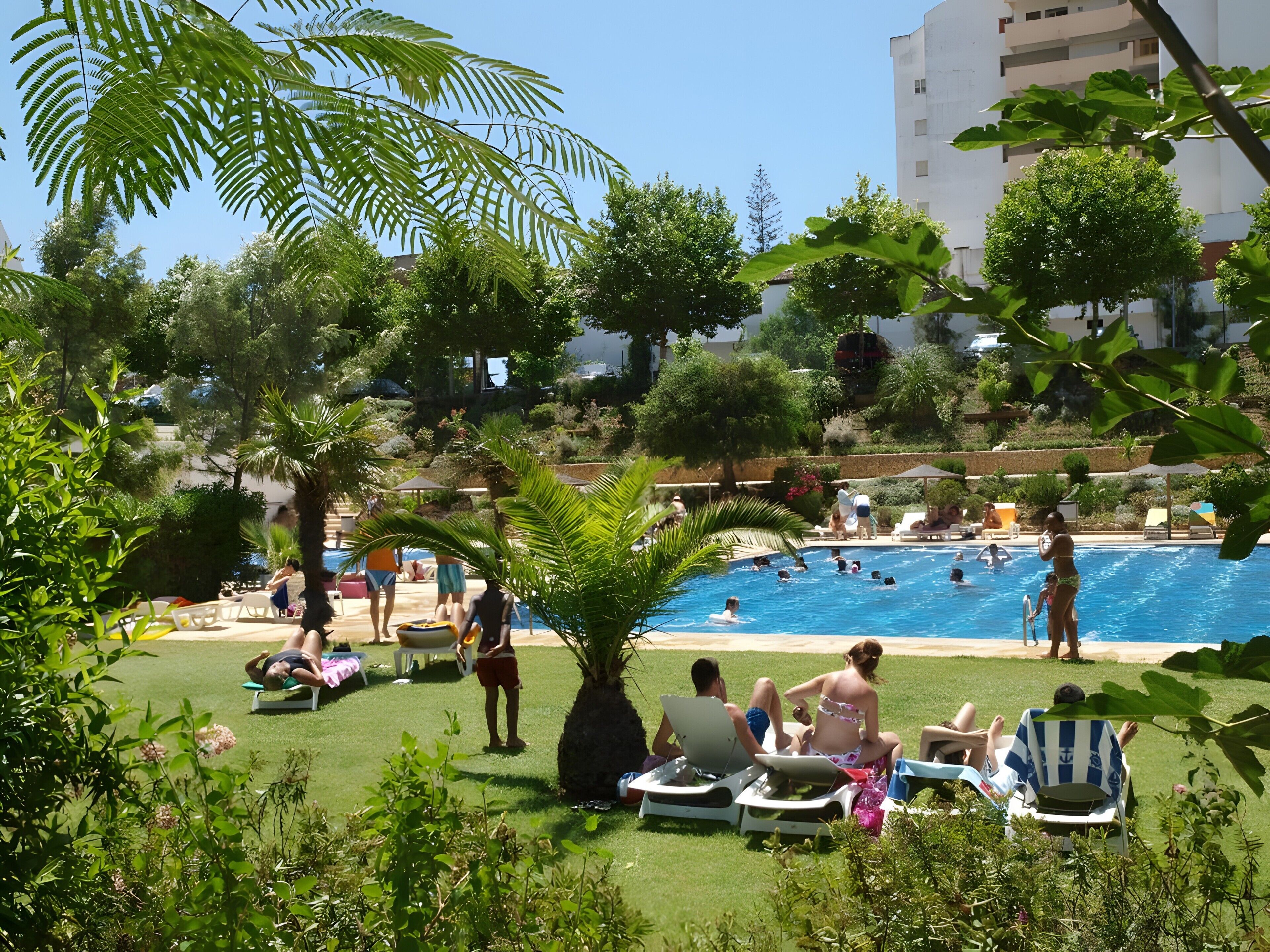 A pool area with lounge chairs and people swimming.