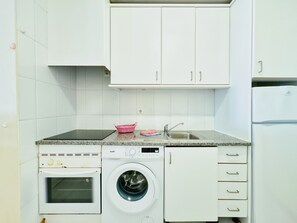 Una cocina compacta con armarios blancos, horno empotrado, lavadora y un lavaplatos.