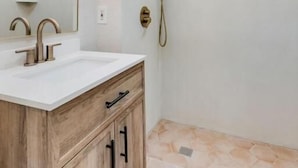 Un baño con tocador de madera, un espejo grande, ducha con cabezal de ducha de mano y suelo de baldosas.