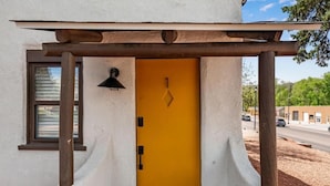 Un edificio con puerta amarilla, una ventana y una estructura de pérgola de madera.