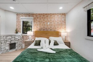 A hotel room with a bed, a nightstand, a lamp, a fireplace, and a patterned wall.
