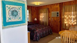 Ein Zimmer mit Holzvertäfelung, einem Bett mit gemustertem Überwurf, einem Sessel und einer Wand-Klimaanlage.
