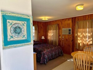 A room with wooden paneling, a bed with a patterned bedspread, a chair, and a wall-mounted air conditioning unit. - Driftwood Resort  (Bull Shoals)