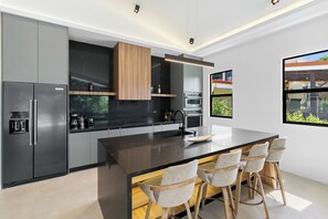 A modern kitchen with a central island, bar stools, built-in appliances, and a large window. - Modern Private Pool Villa near Playas del Coco & Playa Hermosa (Coco)