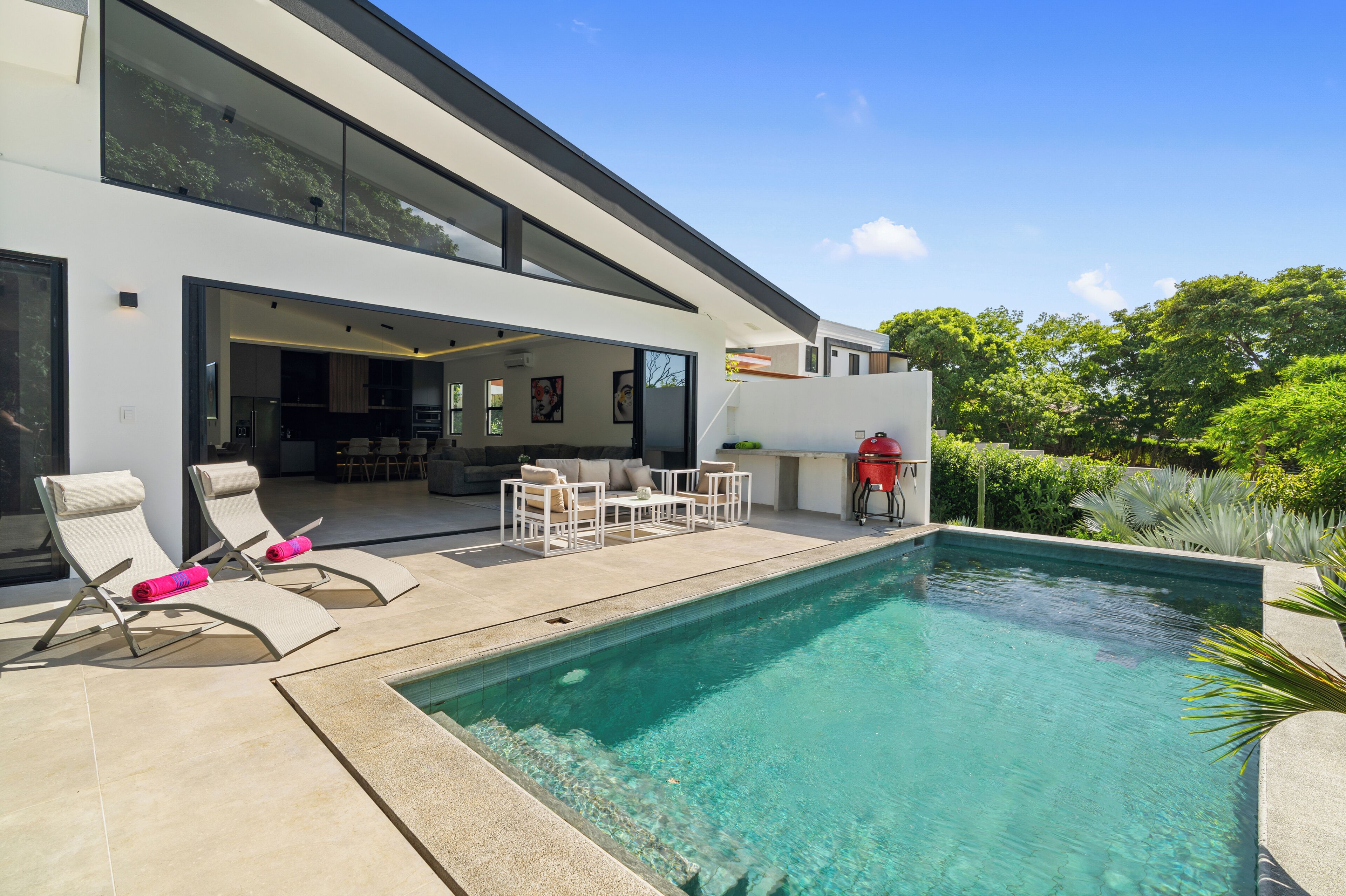 A modern house with a swimming pool, outdoor seating, and a kitchen area.