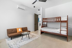 A modern, well-lit room with a bunk bed, a sofa with a cushion, a small round table, and a rug. - Modern Private Pool Villa near Playas del Coco & Playa Hermosa (Coco)