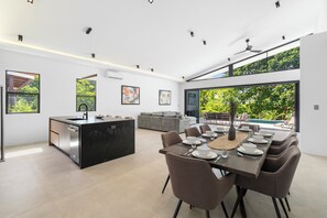 A modern kitchen with a central island, dining area with chairs and table set, and a view of a swimming pool. - Modern Private Pool Villa near Playas del Coco & Playa Hermosa (Coco)