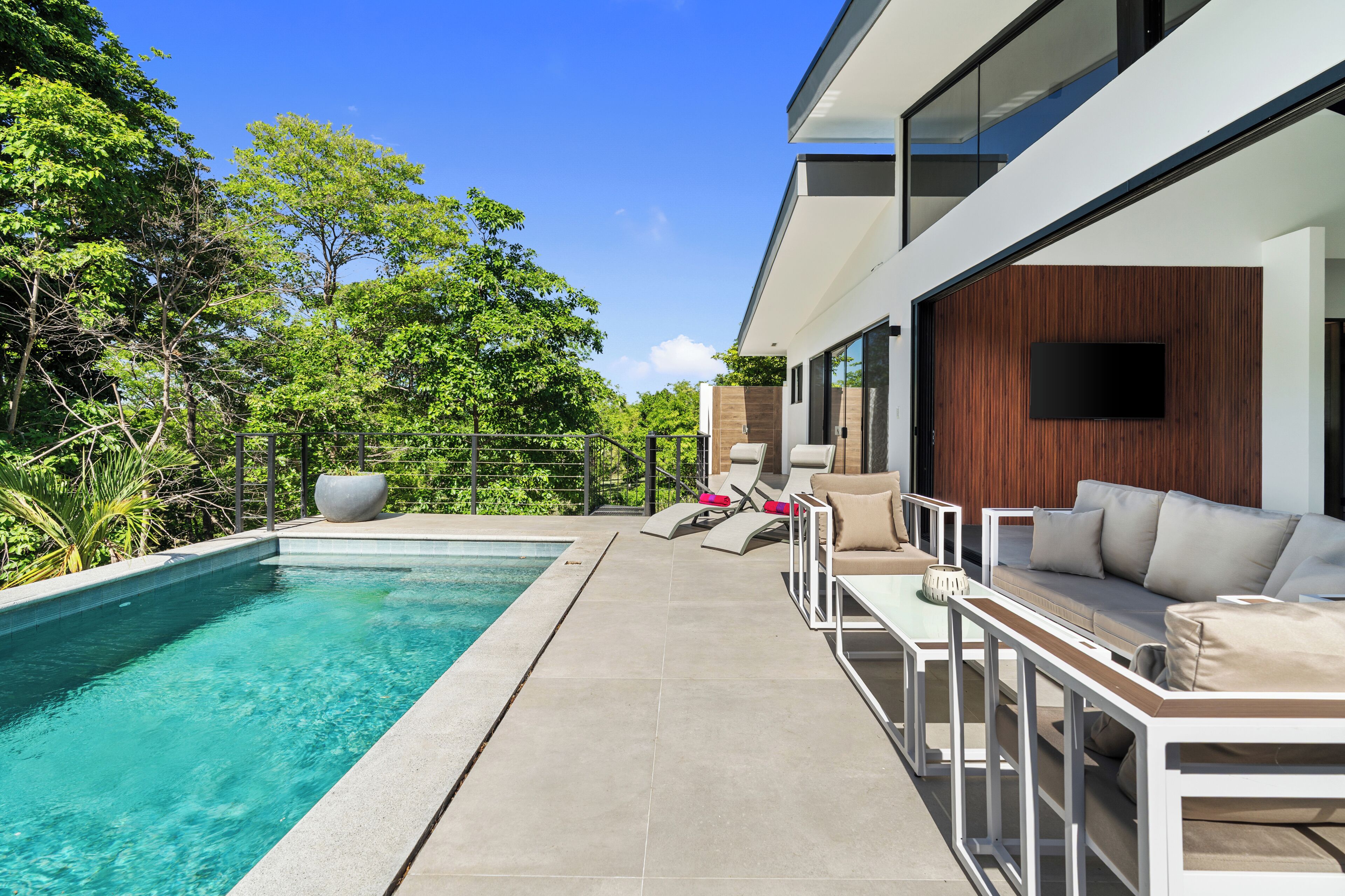 Un espace piscine extérieur moderne, doté d’une piscine à l’eau d’un bleu limpide, de chaises longues et d’un canapé.