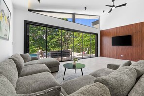 A modern living room with grey sofas, a coffee table, and a TV mounted on a wooden wall. - Modern Private Pool Villa near Playas del Coco & Playa Hermosa (Coco)