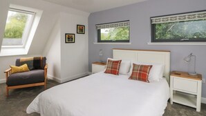 A bedroom with a large bed, two bedside tables, a chair, and a window with a view of greenery. - Taigh Creag Thulach (Taynuilt)