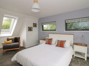 A bedroom with a large bed, two bedside tables, a chair, and a window with a view of greenery. - Taigh Creag Thulach (Taynuilt)